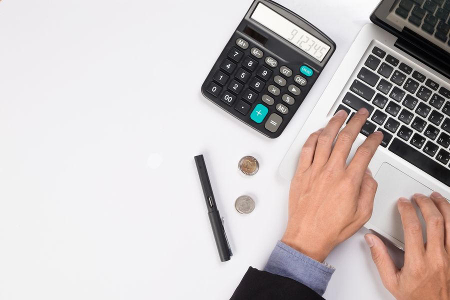 Hands using a calculator beside a laptop and tax paperwork